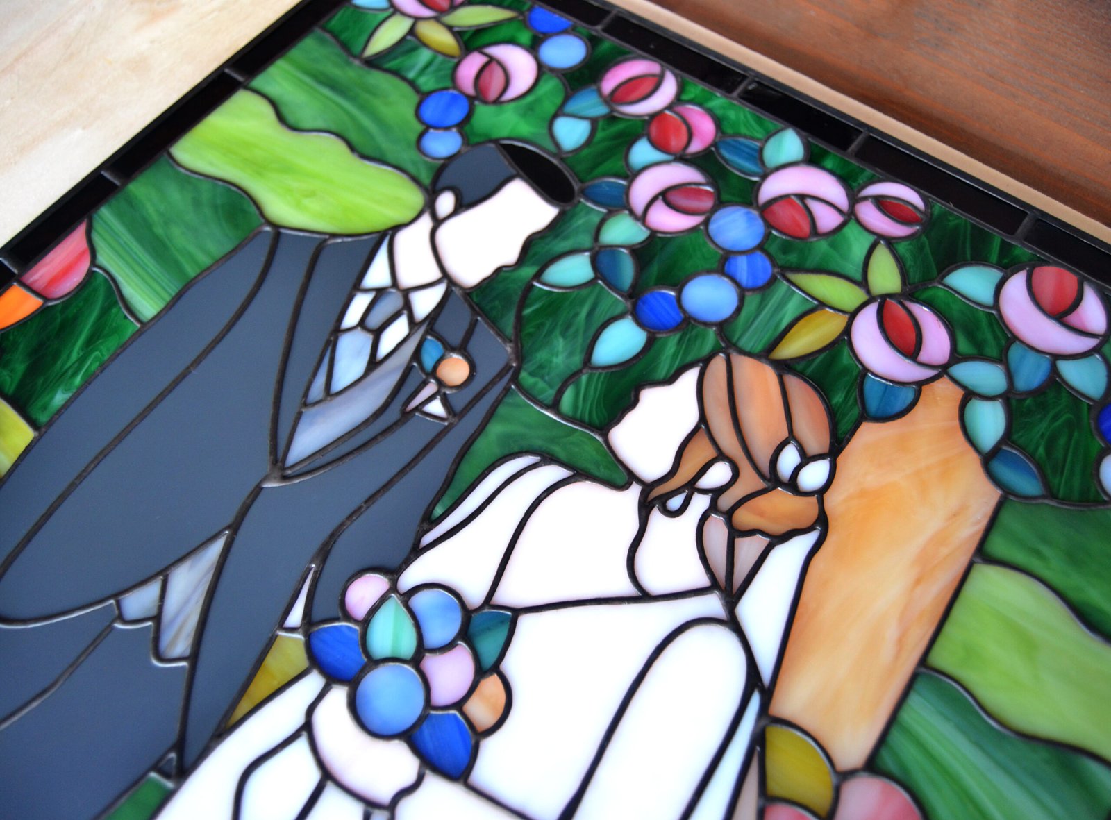 Un vitral artísticamente elaborado que representa a dos personas en su día de boda, con detalles meticulosos que capturan la emoción y la belleza del momento, mientras la luz del sol ilumina los colores vivos y crea un ambiente lleno de amor y alegría.