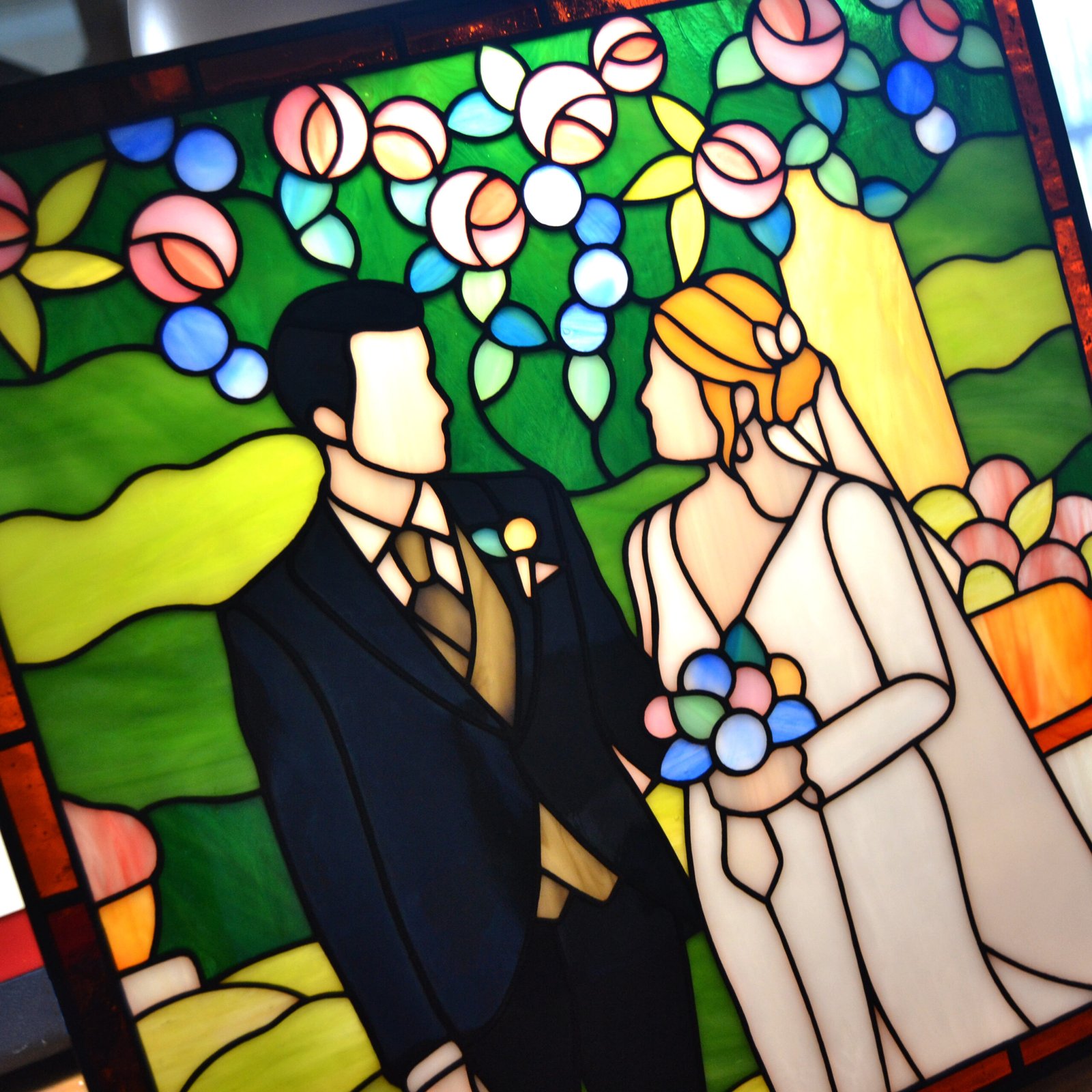 Un vitral artísticamente elaborado que representa a dos personas en su día de boda, con detalles meticulosos que capturan la emoción y la belleza del momento, mientras la luz del sol ilumina los colores vivos y crea un ambiente lleno de amor y alegría.