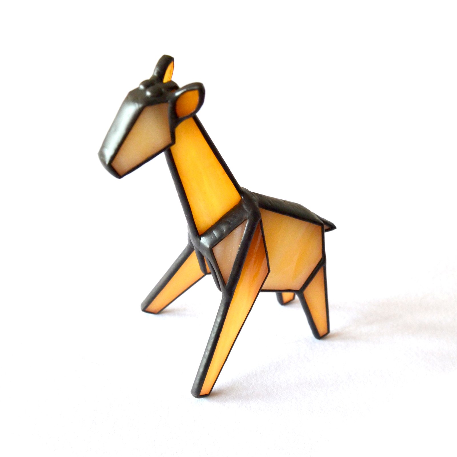 Un vitral en forma de una jirafa, con su cuello largo y elegante, sus manchas distintivas y sus ojos llenos de curiosidad y gracia. La luz del sol ilumina los tonos cálidos y terrosos del vidrio, creando una sensación de serenidad y asombro ante la belleza de la naturaleza.